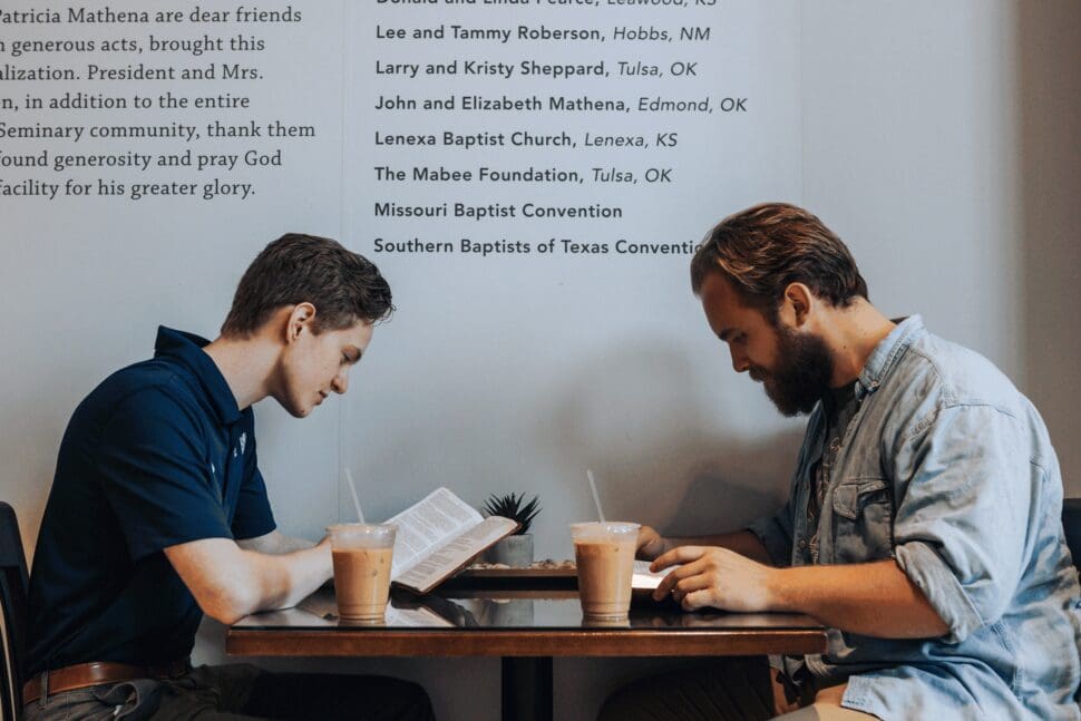 two men reading books with coffee at a table